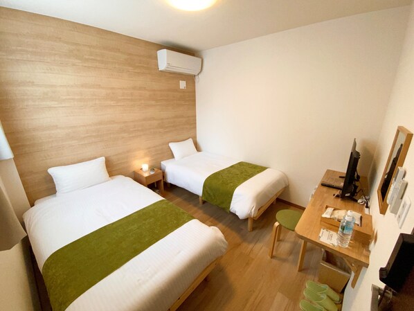 A hotel room with two beds, a desk, a chair, a computer, and an air conditioning unit.