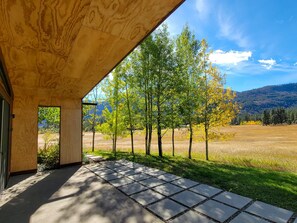 Un espace extérieur abrité, doté d’un chemin de pierre menant à une porte, entouré d’arbres et offrant une vue sur les montagnes.
