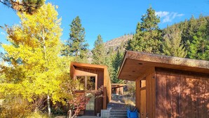 Une cabane moderne, avec une façade en bois, un chemin en béton menant à l’entrée, et une vue sur la forêt et les collines environnantes.