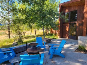 Une terrasse extérieure avec des chaises bleues et un barbecue, entourée d’arbres et bordée d’un bâtiment moderne.