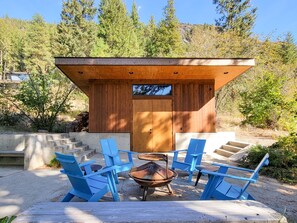 A wooden structure with a door, surrounded by blue chairs and a fire pit.