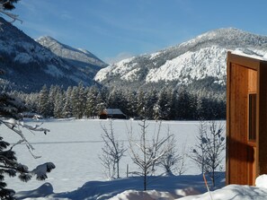 En træhytte med et sneklædt landskab, klar himmel og bjerge i baggrunden.