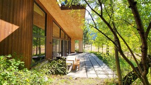 Un bâtiment moderne doté de grandes fenêtres et d’une façade en bois, entouré d’arbres et bordé d’un chemin pavé.