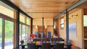 Un espace de salle à manger moderne, doté d’une longue table, de nombreuses chaises, de luminaires suspendus et de grandes fenêtres offrant une vue sur l’extérieur.