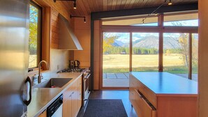 Une cuisine moderne dotée de meubles en bois, d’appareils électroménagers en acier inoxydable et de grandes fenêtres offrant une vue sur un paysage montagneux.