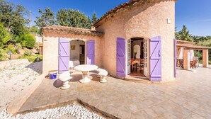 Un bâtiment de style rustique doté d’un patio carrelé, d’une table ronde et de volets violets.