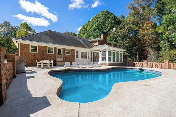 Ein Haus mit Swimmingpool, Ziegelaußenwand und überdachter Terrasse.