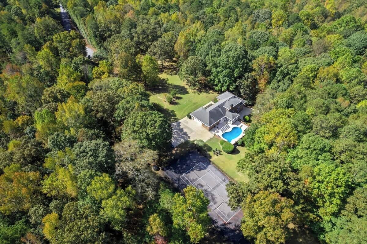 Vista aérea de una casa rodeada de bosque denso, con piscina visible y entrada para vehículos.