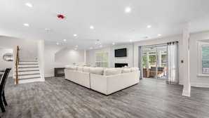 A spacious living room with a large sectional sofa, a staircase, and a flat-screen TV mounted on the wall. - Grand Retreat: Luxury Vacation for Large Groups (Fayetteville)