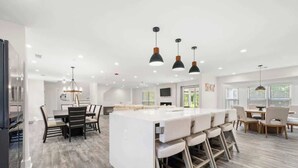 A spacious kitchen with a central island, pendant lighting, and a dining area with chairs and a table. - Grand Retreat: Luxury Vacation for Large Groups (Fayetteville)