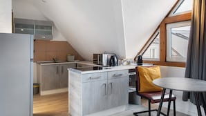 A compact kitchen with a built-in stove, a microwave, and a coffee maker. There is a dining area with a table and a chair. - Studio Apartment 'Vogelsberger Bett Die 2' with Wi-Fi (Alsfeld)