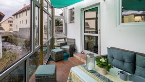 A balcony with wicker furniture, a table with a patterned tablecloth, and a view of buildings. - Holiday Home 'Vogelsberger Bett Köddingen' with Private Terrace, Private Garden and Wi-Fi (Feldatal)