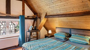 A bedroom with a sloped ceiling, a bed with striped bedding, a bedside lamp, and a window with curtains. - Holiday Home 'Vogelsberger Bett Köddingen' with Private Terrace, Private Garden and Wi-Fi (Feldatal)
