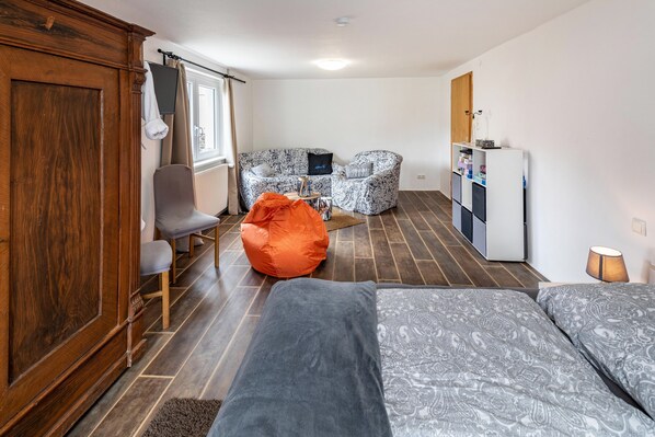 Une pièce de taille modeste comprenant un lit, un canapé, une chaise, une petite table et un coin cuisine.