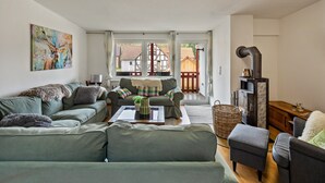 A living room with a sofa, armchairs, a coffee table, a fireplace, and a view of the outside. - Holiday Home 'Vogelsberger Bett Köddingen' with Private Terrace, Private Garden and Wi-Fi (Feldatal)