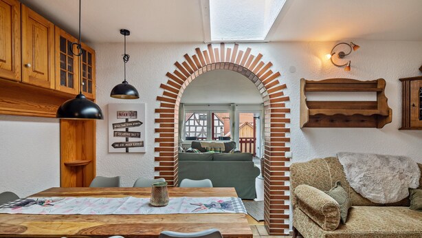 A dining area with a wooden table and chairs, a brick archway, and a sofa in the background. - Holiday Home 'Vogelsberger Bett Köddingen' with Private Terrace, Private Garden and Wi-Fi (Feldatal)