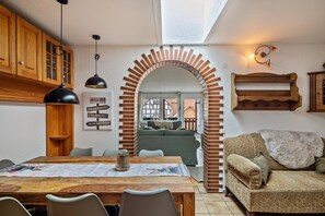 A dining area with a wooden table and chairs, a brick archway, and a sofa in the background.