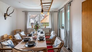 A dining area with a long table set for four, surrounded by wicker chairs with red cushions, a fur throw, and a mounted deer skull on the wall. - Holiday Home 'Vogelsberger Bett Köddingen' with Private Terrace, Private Garden and Wi-Fi (Feldatal)