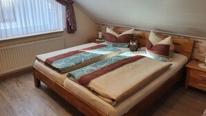 Een slaapkamer met een houten bed, beddengoed met een patroon, een nachtkastje, een raam met gordijnen en een bakstenen muur.