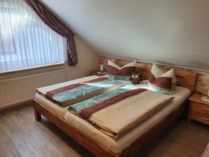 Ein Schlafzimmer mit einem hölzernen Bett, gemusterten Betttextilien, einem Nachttisch, einem Fenster mit Vorhängen und einer Ziegelwand.