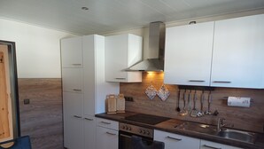 Een moderne keuken met witte kasten, een houten aanrechtblad en een fornuis. Er staat een eettafel met een mand vol fruit.