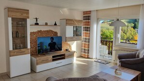 Een moderne woonkamer met een televisie, houten meubels en een balkon met uitzicht.