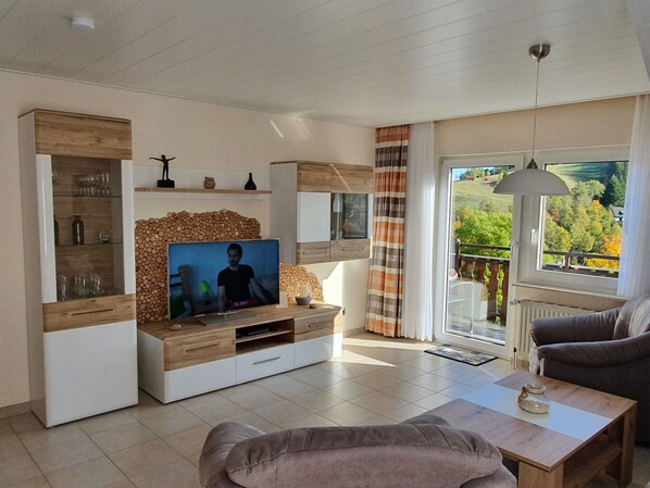 A modern living room with a TV, wooden furniture, and a balcony with a view.