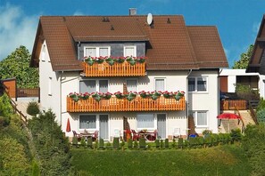 Una casa de dos pisos con un balcón, un comedor con mobiliario exterior y un jardín.