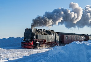 Una locomotora de vapor con un vagón rojo avanzando por un paisaje nevado.