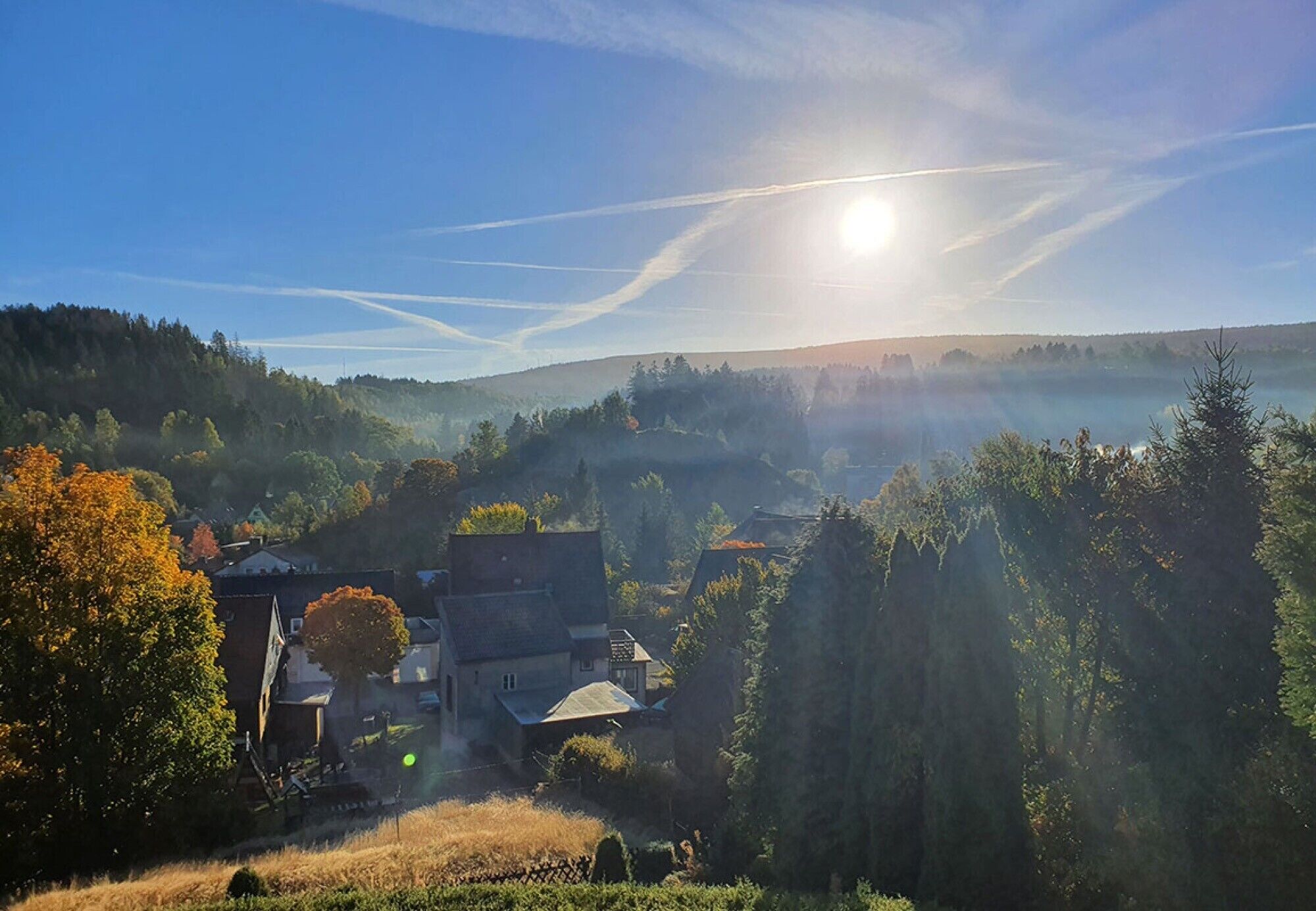 Paisaje rural con cielo despejado, un pueblo bañado por el sol y una iglesia destacada.