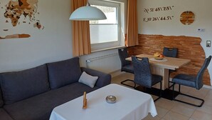 A room with a sofa, a dining table with chairs, a map on the wall, and a clock. - Apartment No. 2: Brand-New Flat in Altenau – Near Spa, Prime Location with Sauna, Wi-Fi & EV Charging (Altenau)