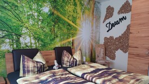 A bedroom with a bed, pillows, a nightstand, a wall tapestry, and a decorative wall piece. - Apartment No. 2: Brand-New Flat in Altenau – Near Spa, Prime Location with Sauna, Wi-Fi & EV Charging (Altenau)
