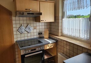 Une cuisine de taille réduite, équipée d’une cuisinière, d’un four, de meubles en bois et d’une fenêtre avec des rideaux.