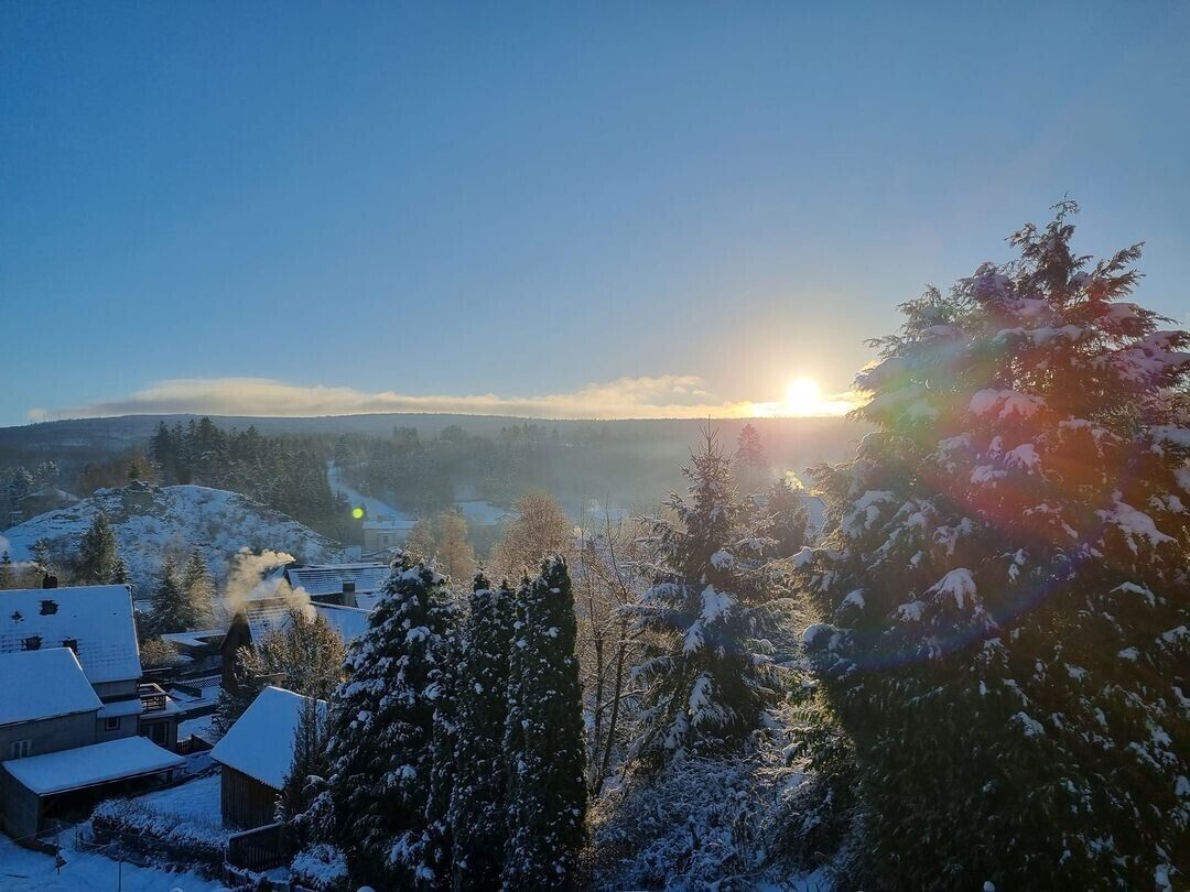 Een besneeuwd landschap met een zonsopgang, huizen en bomen.