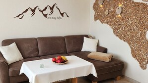 Un sofá de cuero marrón con un mantel blanco, un frutero y una pared con diseño de montaña y un arte mural con textura de madera.