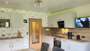 Een moderne keuken met witte kastjes, een houten eettafel en een televisie boven de toonbank.