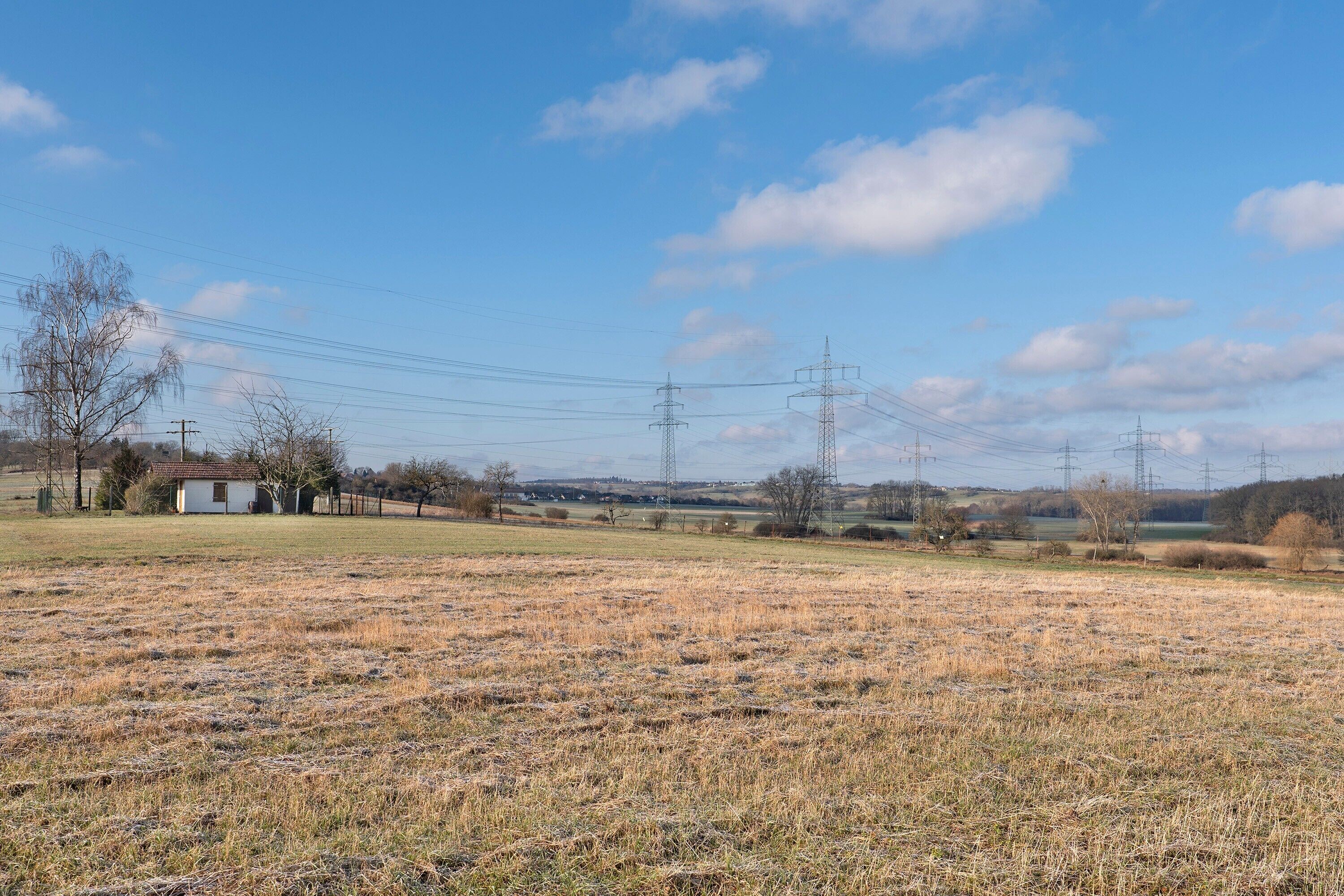 A rural landscape with a small white building, power lines, and a clear sky.
