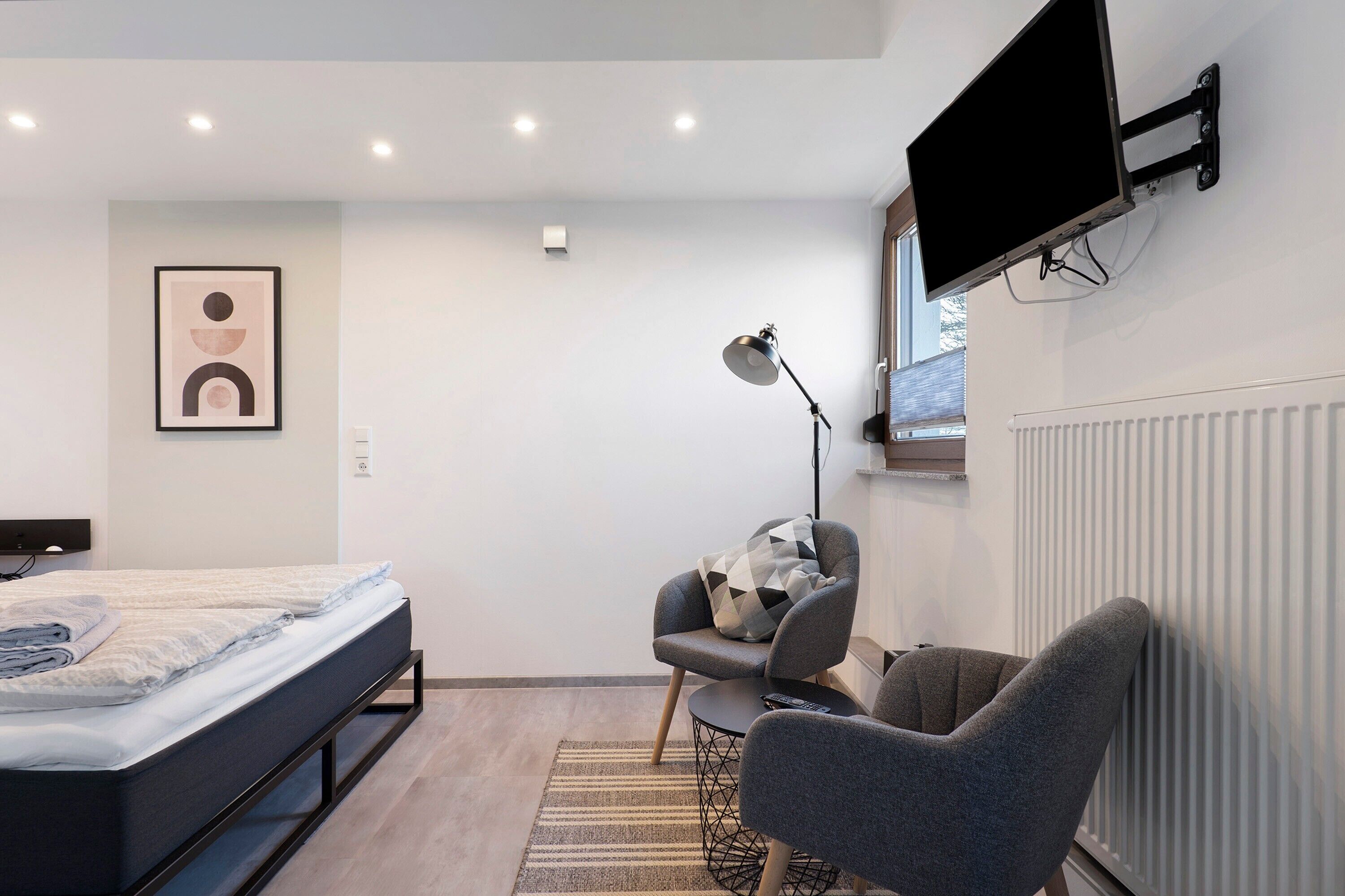 Un dormitorio moderno con cama, escritorio, silla, televisor y radiador.