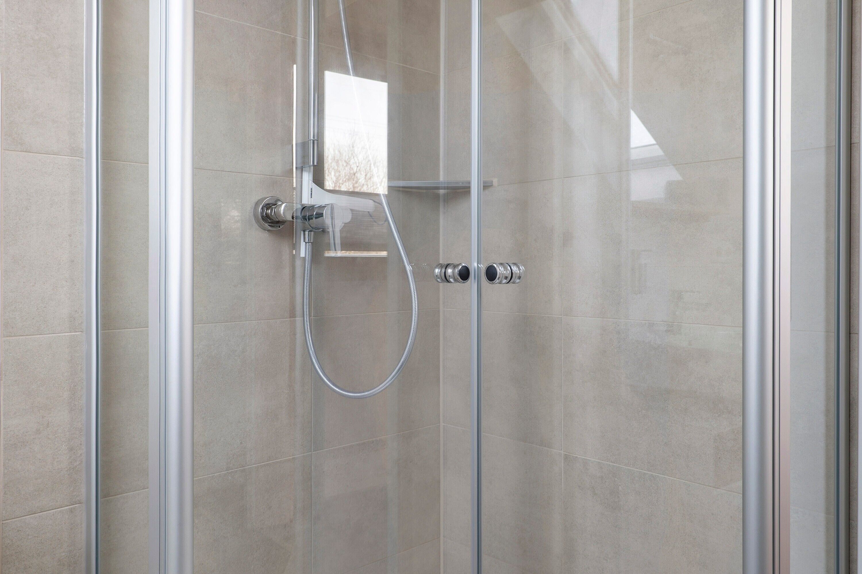 Une douche fermée par des parois en verre, dotée d’un pommeau de douche à main et d’un panneau de commande fixé au mur.