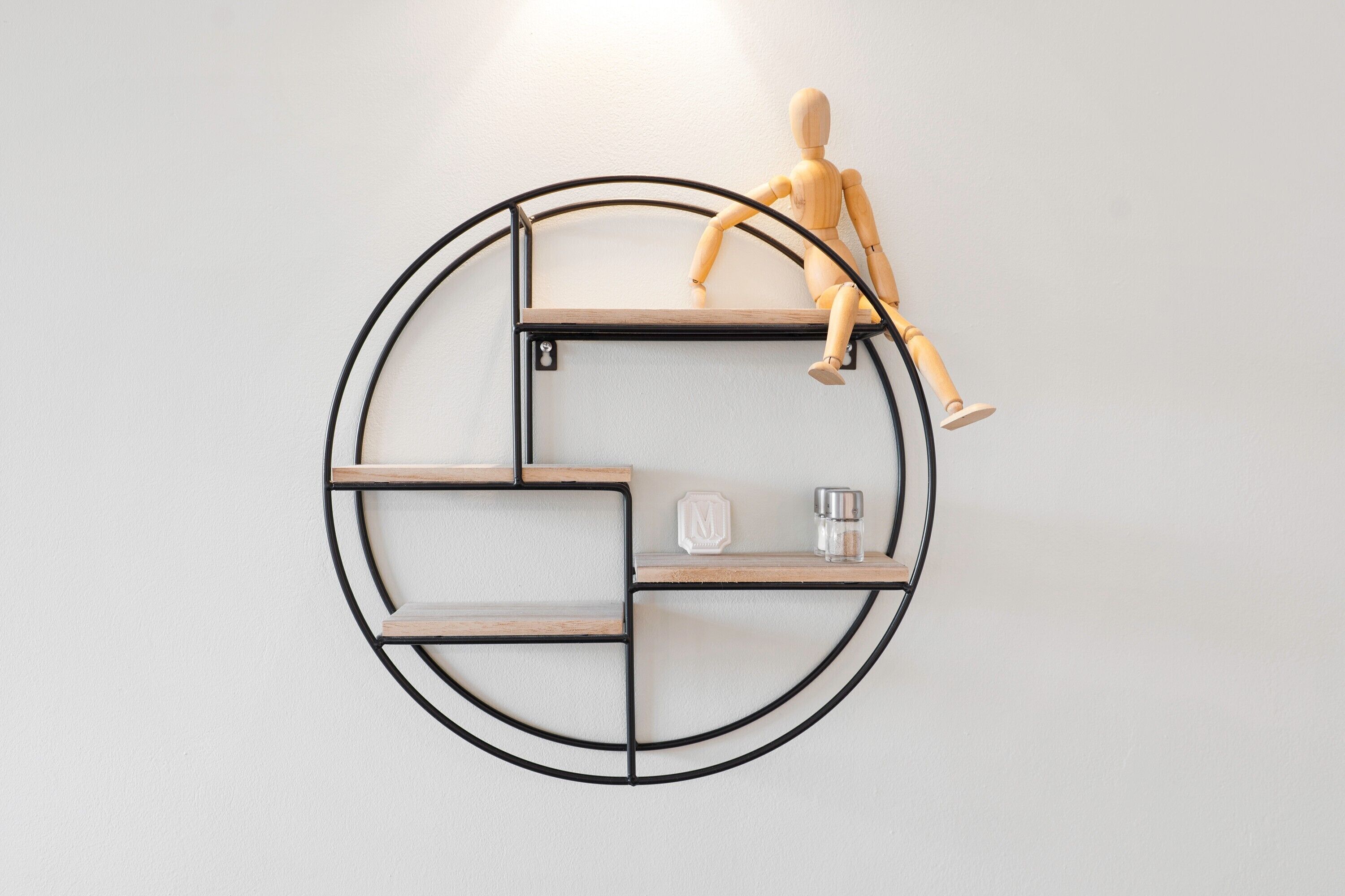 Une étagère circulaire fixée au mur, dotée de compartiments, un mannequin en bois et un petit récipient en verre.
