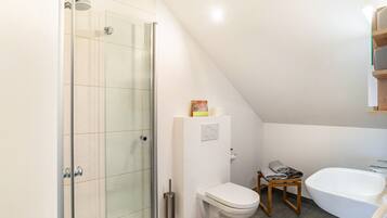Ein Badezimmer mit Duschkabine aus Glas, einer weißen Toilette, einem hölzernen Hocker und einer weißen Badewanne.