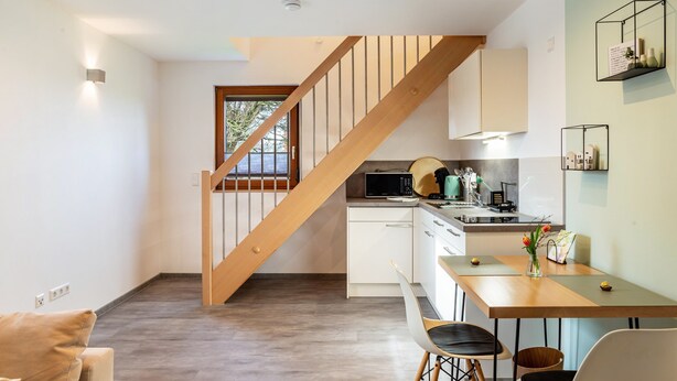 A modern kitchen with wooden staircase, white cabinets, and a dining area with a table and chairs. - Apartment 'Kräuterglück' with Shared Garden and Wi-Fi (Ötisheim)