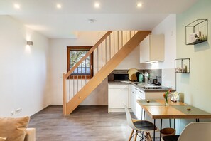A modern kitchen with wooden staircase, white cabinets, and a dining area with a table and chairs.