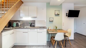 A modern kitchen with white cabinets, a wooden staircase, a dining area with a table and chairs, and a mounted TV. - Apartment 'Kräuterglück' with Shared Garden and Wi-Fi (Ötisheim)