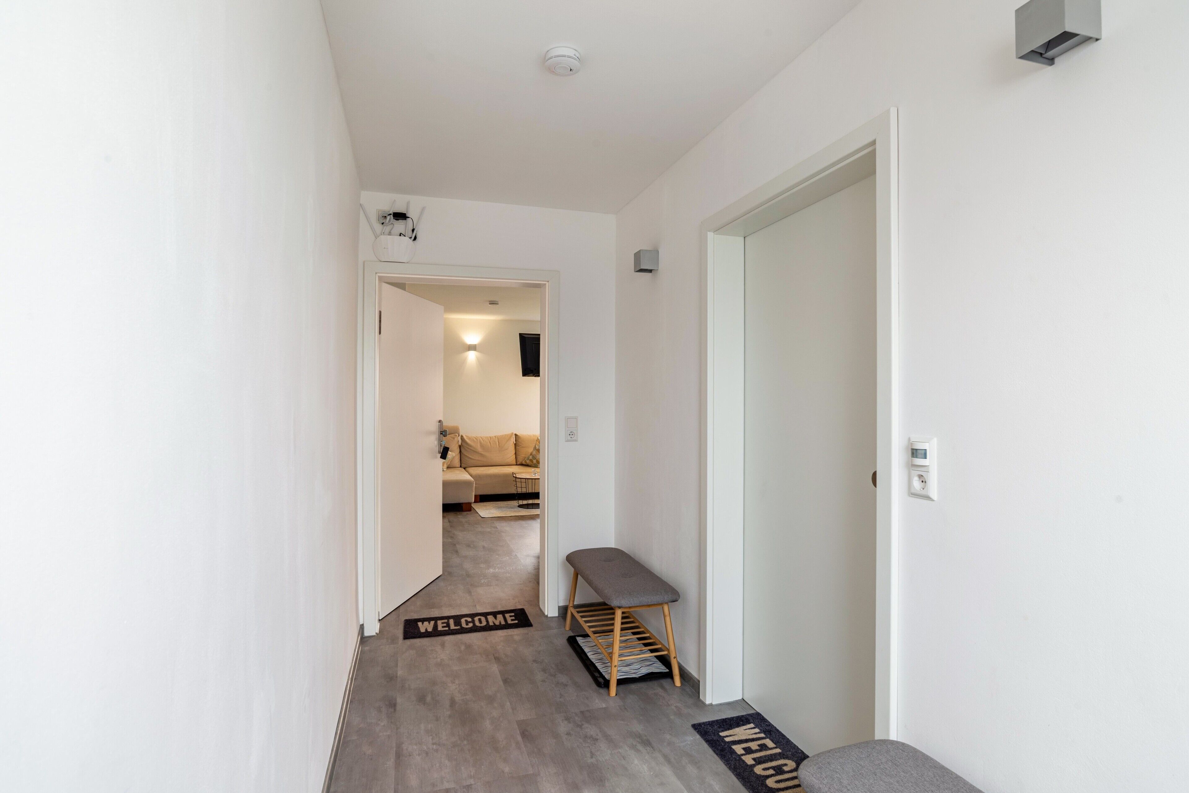 A hallway with a bench, a welcome mat, and a door leading to a living area.