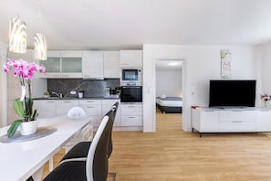 A modern kitchen with white cabinets, a dining area with a white table and chairs, and a living area with a TV and white entertainment unit. - Apartment "Dußlingen" with Private Terrace & Wi-Fi (Dußlingen)