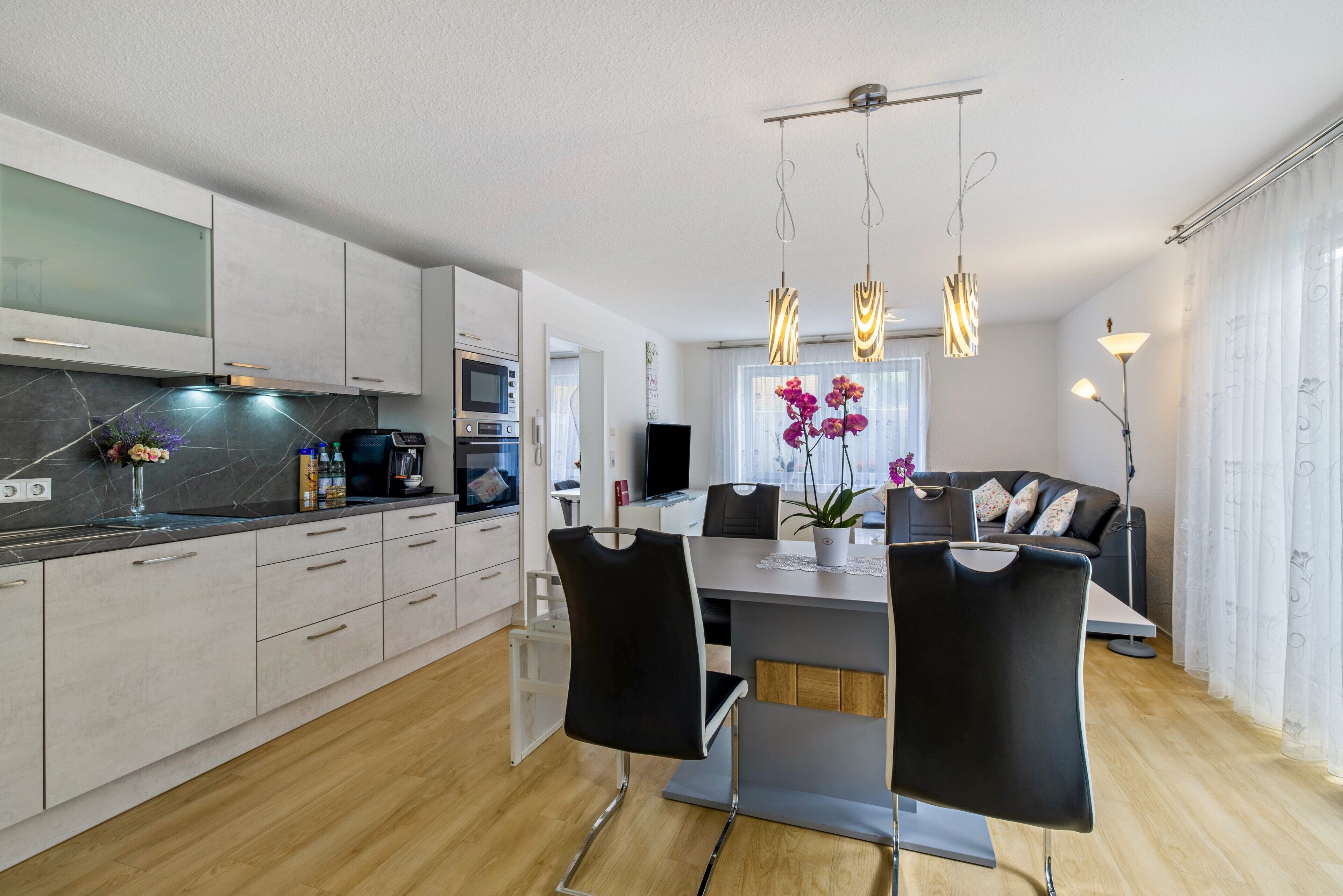 A modern kitchen with a dining area, a flat-screen TV, and a sofa in the living room.