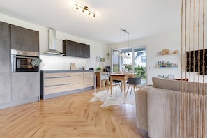 Una cocina moderna con horno integrado, un comedor con mesa y sillas, y una sala de estar con sofá.