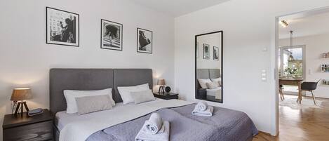 A modern bedroom with a large bed, bedside tables, a mirror, and framed pictures on the wall.