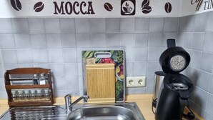 A kitchen with a stainless steel sink, a coffee maker, a wooden spice rack, and a coffee-themed wall decoration. - Studio Apartment "Kuckuck" with Wi-Fi (Ohlsbach)